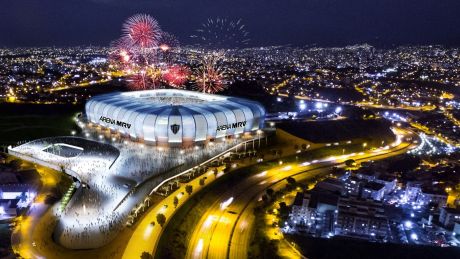 Vista aérea noturna da Arena MRV iluminada com fogos e público no entorno