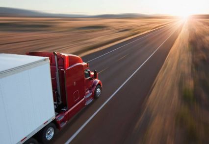 Caminhão vermelho trafegando em rodovia ao pôr do sol