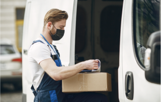 Entregador com máscara manuseando caixa ao lado de van