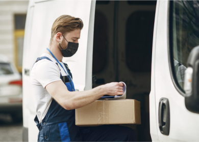 Entregador com máscara manuseando caixa ao lado de van