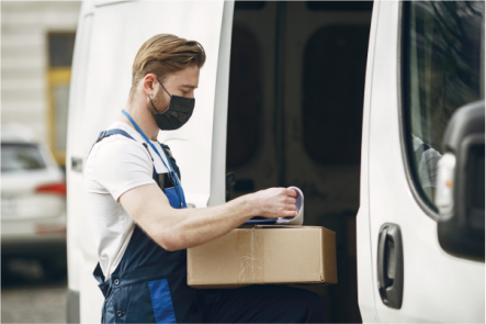 Entregador com máscara manuseando caixa ao lado de van