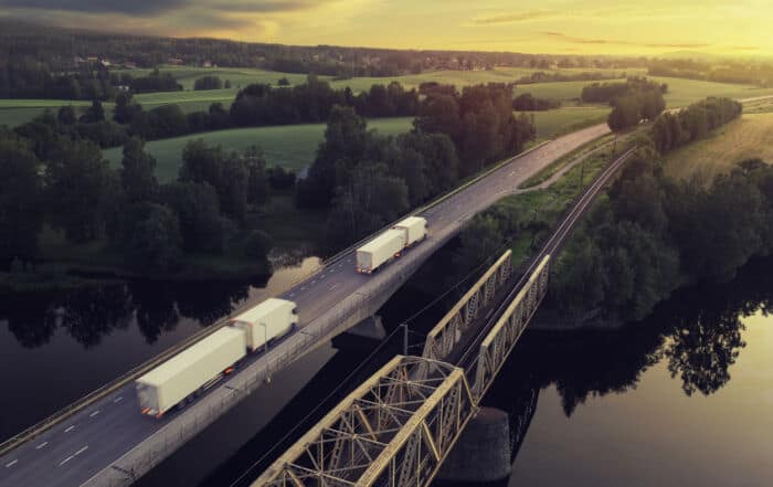 Caminhões em ponte sobre rio em paisagem rural ao pôr do sol