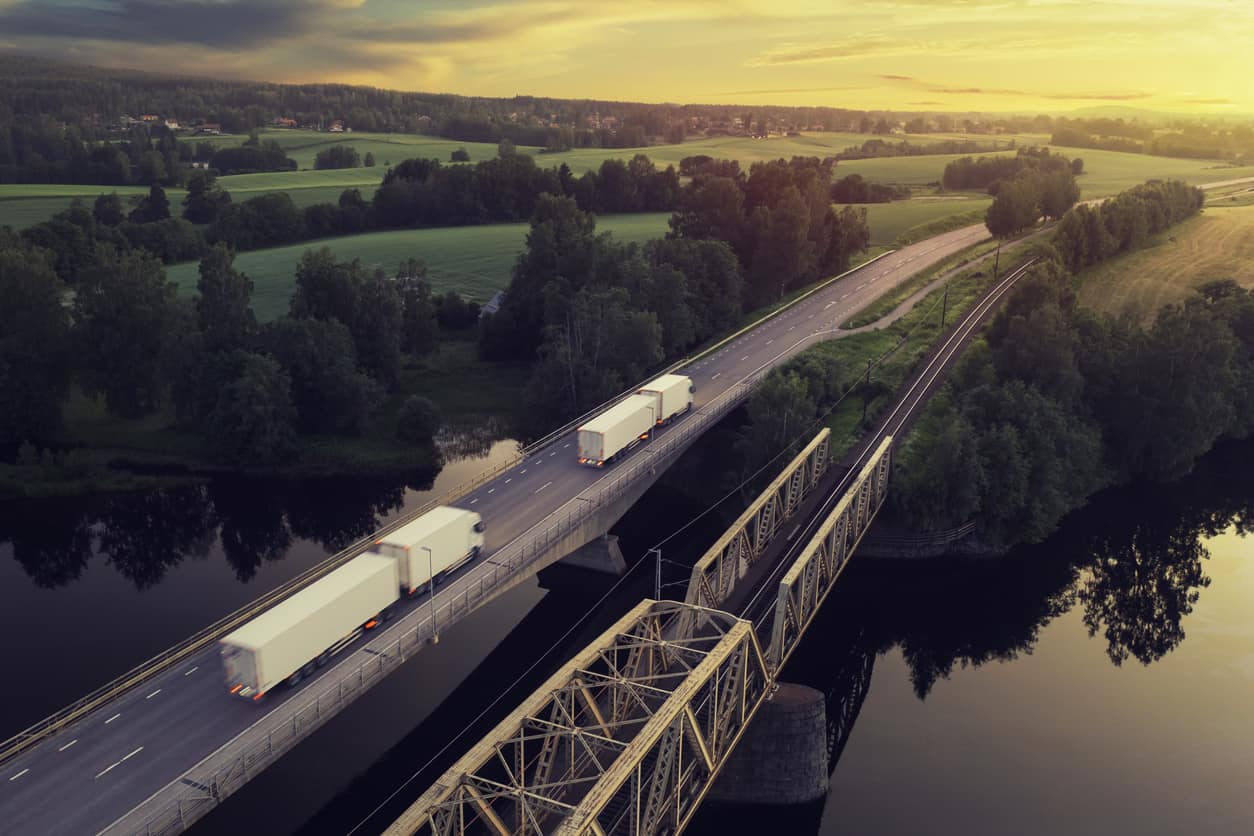 Caminhões em ponte sobre rio em paisagem rural ao pôr do sol